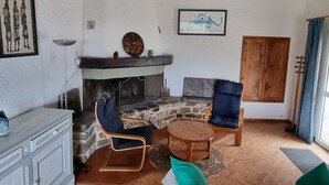 Ein gemütliches Zimmer mit Kamin, Steinwand, Holzbalkendecke, einem Esstisch mit Stühlen und einer großen Holztür.