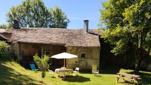 Una casa de piedra rústica con techo inclinado, un pequeño jardín con mesa y sillas, y una mesa de picnic.
