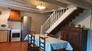 Una cocina con mesa, sillas, una escalera y un microondas.