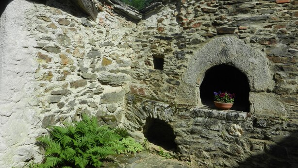 Un edificio de piedra con un pequeño ventanal de arco y una planta en maceta.