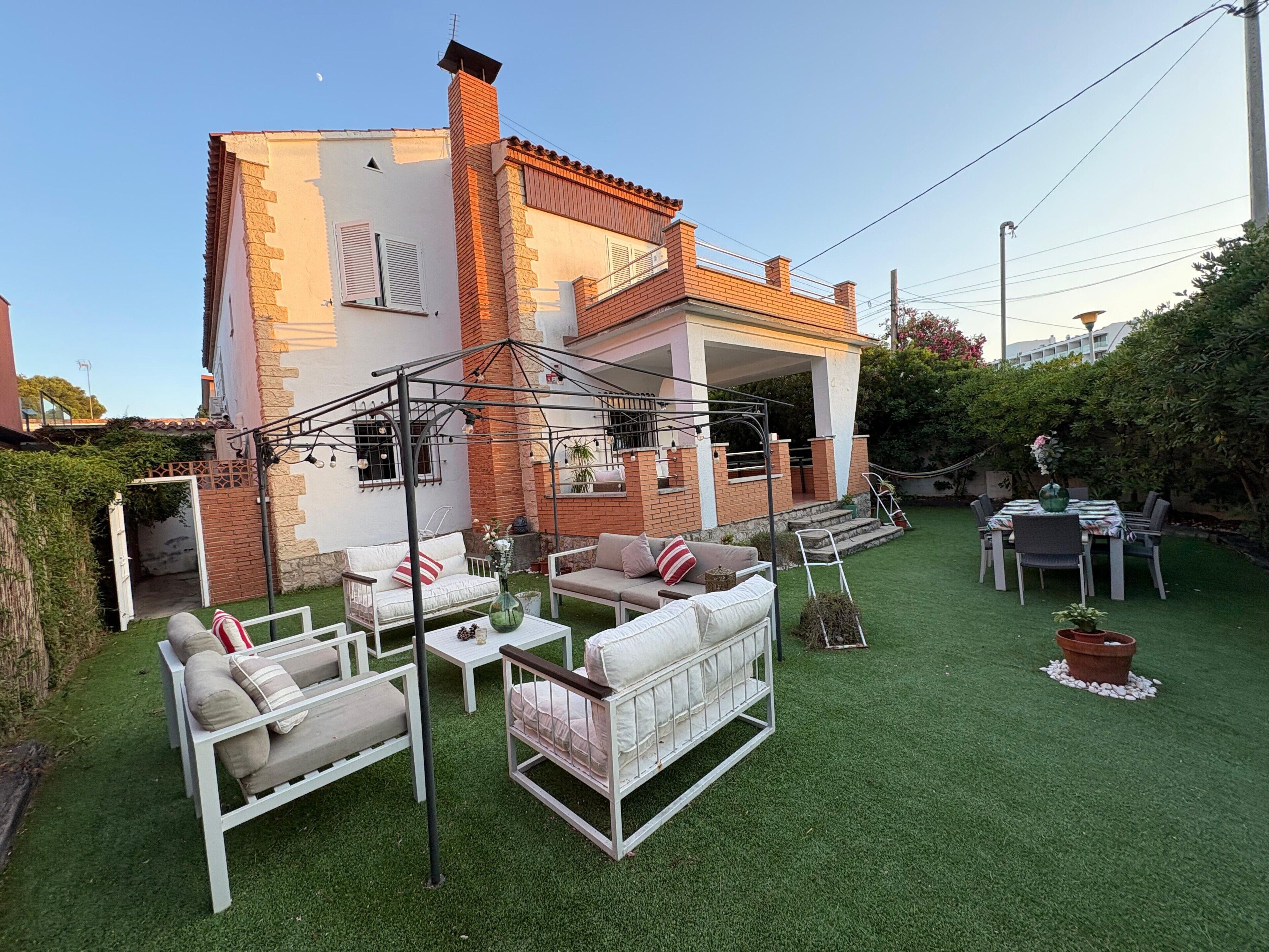 Una casa con un patio amoblado, con mobiliario exterior, un espacio de estar techado y un césped cuidado.
