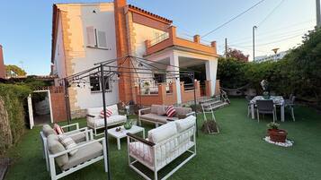 Una casa con un patio amoblado, con mobiliario exterior, un espacio de estar techado y un césped cuidado.