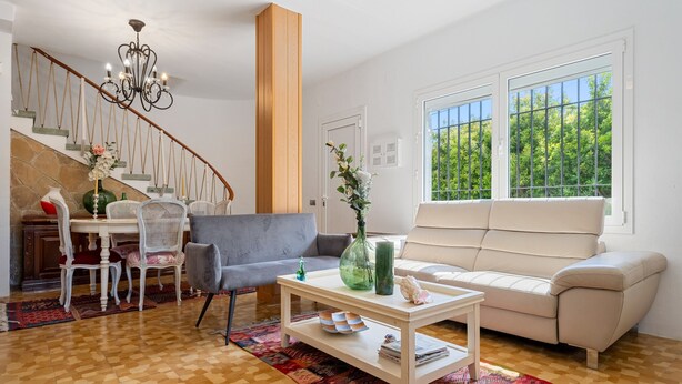 A living room with a staircase, a sofa, a coffee table, and a dining area with chairs and a table. - Chalet '50 M to the Beach' with Private Terrace, Wi-Fi and Air Conditioning (Comarruga)