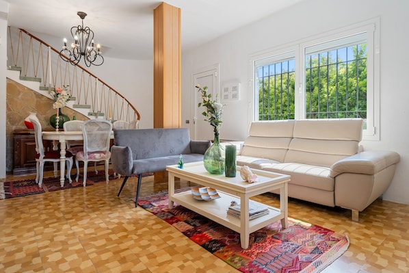 A living room with a staircase, a sofa, a coffee table, and a dining area with chairs and a table.