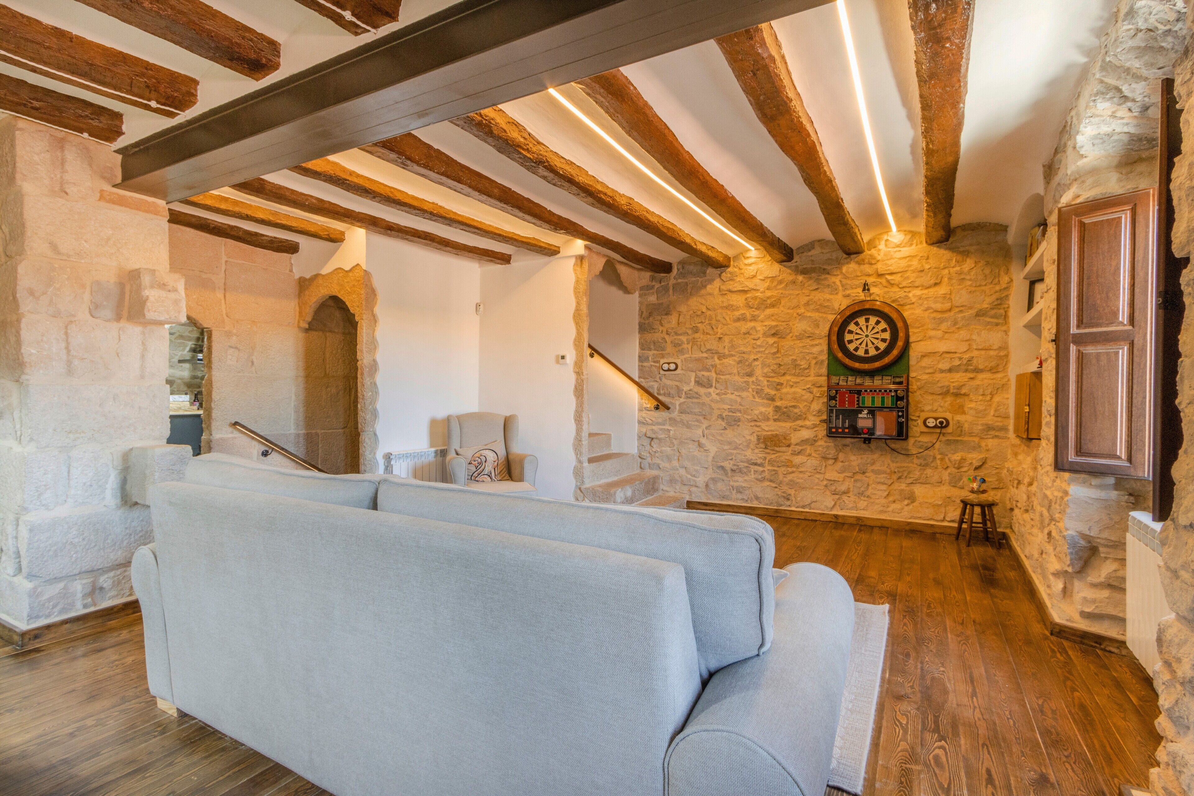 Una habitación con pared de piedra, un dardo, un sofá y una escalera.