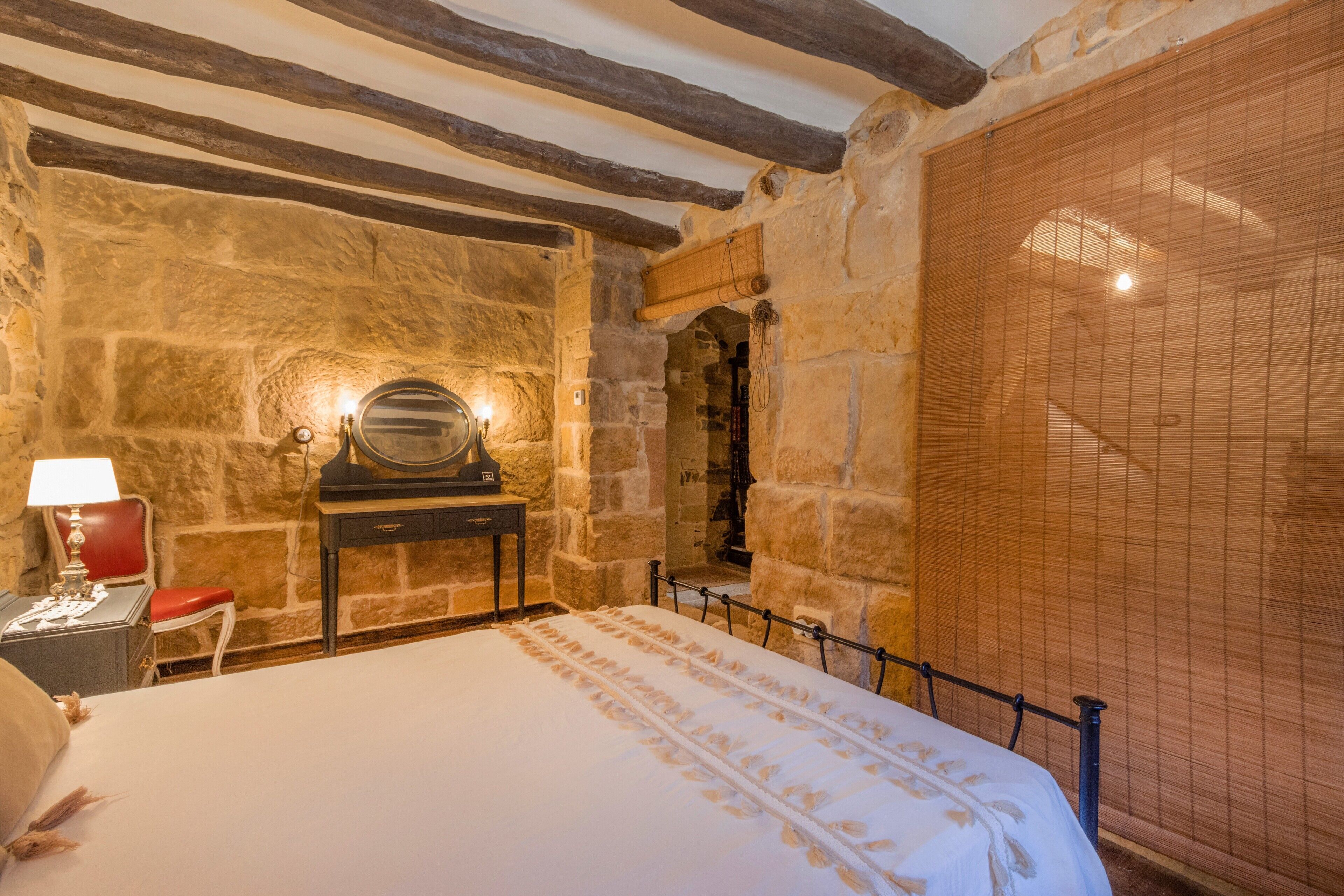 Una stanza con pareti in pietra, un letto, un pianoforte e una sedia rossa.