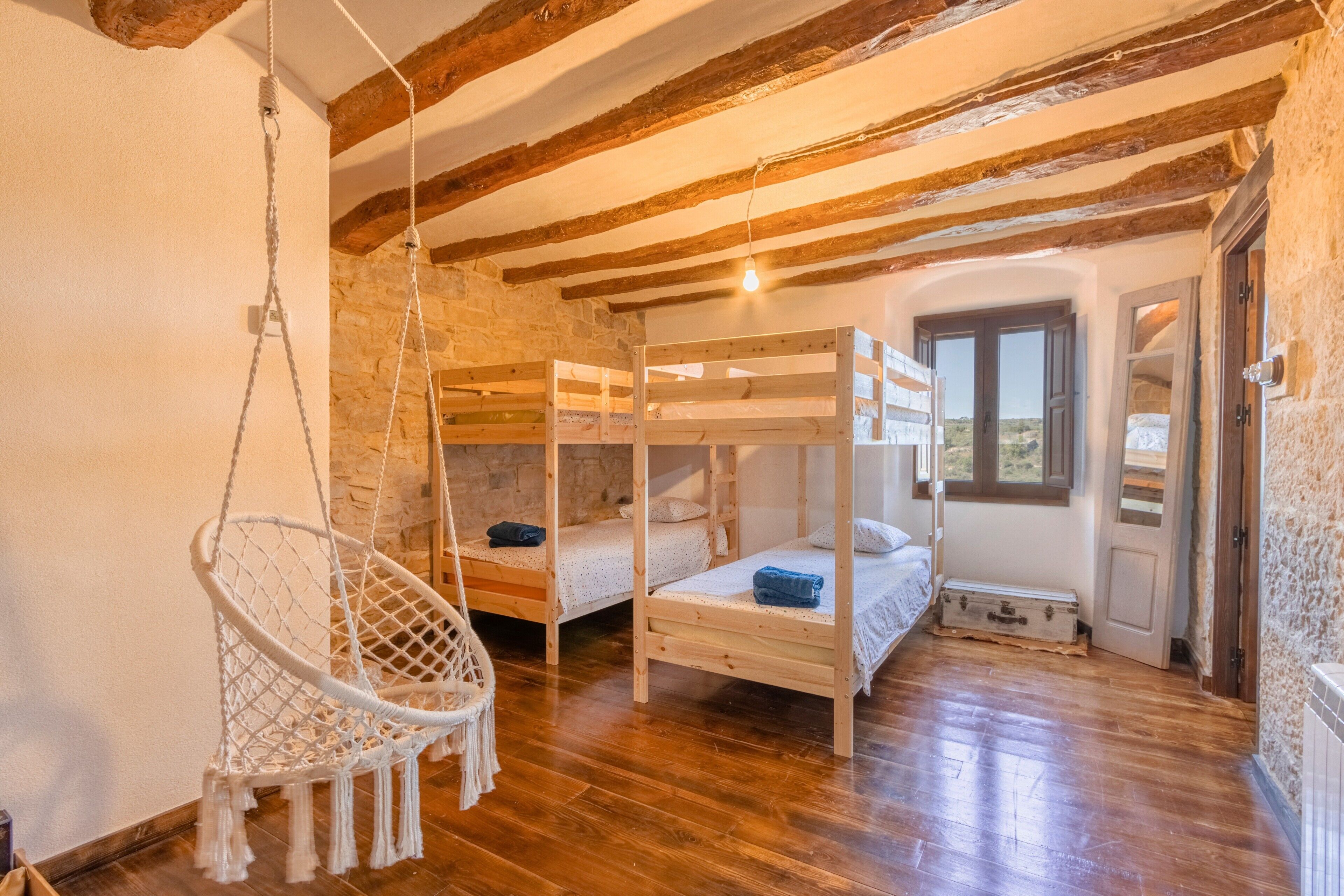Een kamer met houten stapelbedden, een hangstoel en een stenen muur.