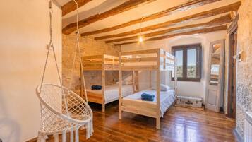 Een kamer met houten stapelbedden, een hangstoel en een stenen muur.