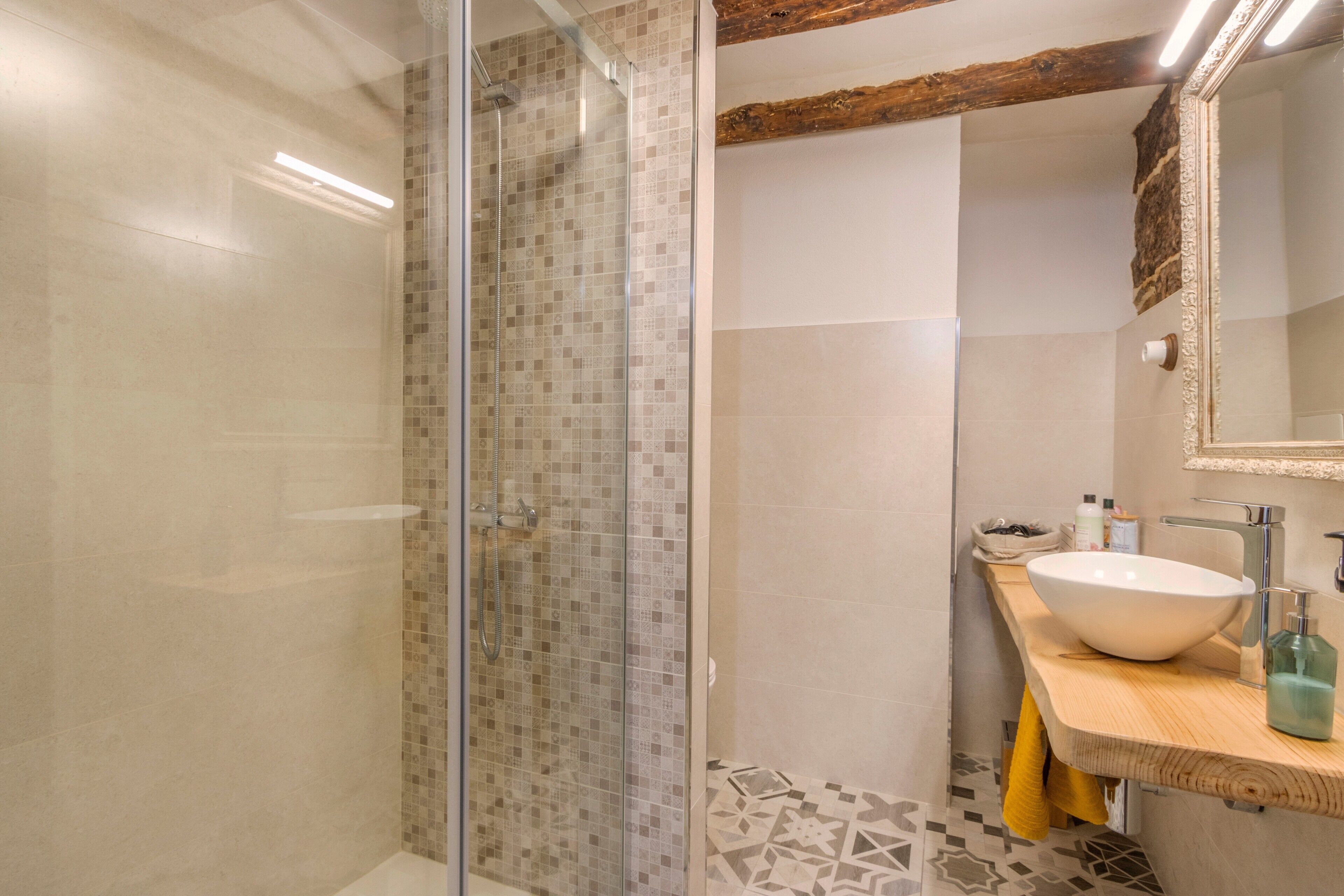A modern bathroom with a glass shower enclosure, a white sink with a vessel basin, and a wooden countertop.