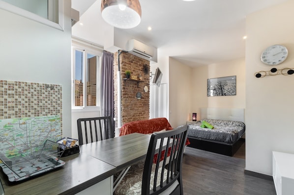 A modern room with a dining table, chairs, a bed, a map on the table, and a clock on the wall.