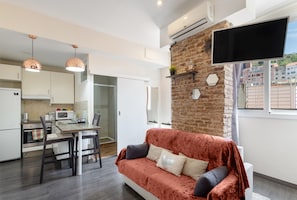 A modern kitchen with a dining area, a sofa, and a TV mounted on a brick wall.