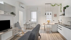 Eine moderne Küche mit weißen Schränken, ein Essbereich mit Tisch und Stühlen, ein Sofa und ein Fernseher.