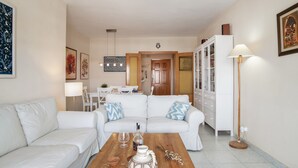 Una sala de estar con un sofá blanco, una mesa de centro de madera y un comedor al fondo.
