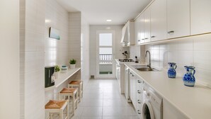 Una cocina estrecha con armarios blancos, una lavadora y dos jarrones azules sobre la encimera.