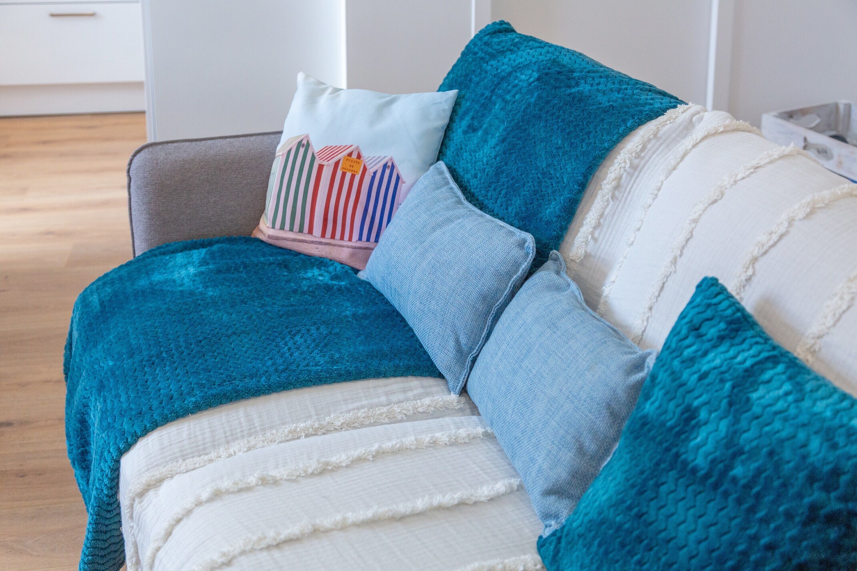 Un canapé avec des coussins turquoise et blancs, un coussin à rayures et un coussin bleu clair.