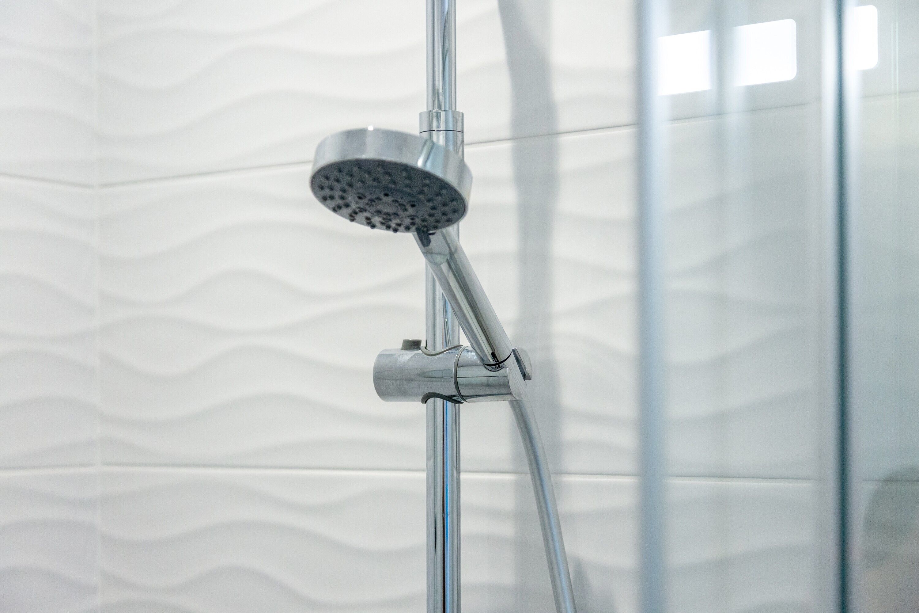 A showerhead attached to a chrome fixture in a bathroom with a wavy tile pattern on the wall.