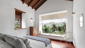 Une chambre à coucher avec un lit, une fenêtre donnant sur un paysage verdoyant, une chaise et une commode.