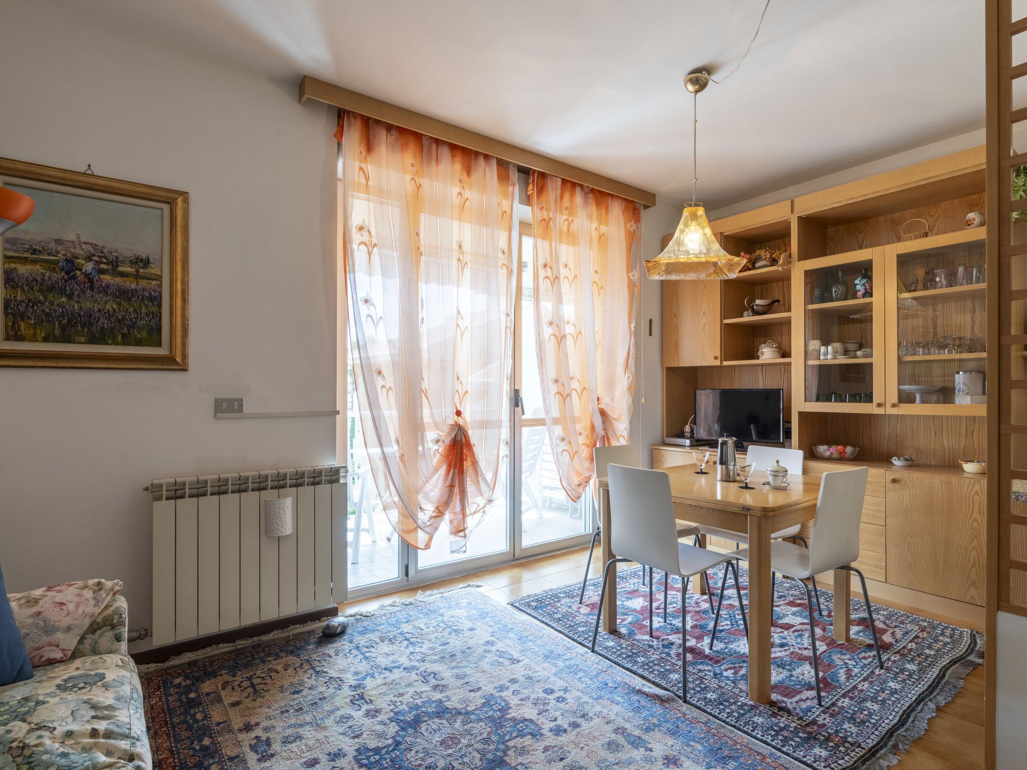 A dining area with a table, chairs, a hanging light fixture, and a view of the outdoors through sheer curtains.
