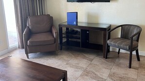 Una sala de estar con un televisor de pantalla plana, un sillón de cuero marrón, un sillón a rayas, una mesa de centro de vidrio y una lámpara.