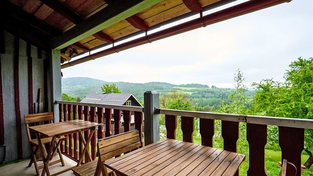 A covered outdoor seating area with wooden tables and chairs, overlooking a scenic landscape with hills and trees. - Jizerka by Interhome (Tanvald)