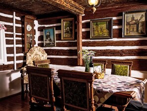 A rustic dining room with wooden walls, a wooden dining table, and chairs. There are framed pictures on the walls, a clock, and a vase with flowers on the table. - Jizerka by Interhome (Tanvald)