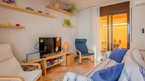 A modern living room with a TV, seating, shelves, and a view to the outside. - Costabravaforrent Can Riera (l'Escala)