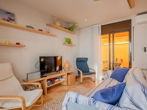 Een woonkamer met een televisie, een bank, een stoel en een zichtbare eethoek door een glazen deur.
