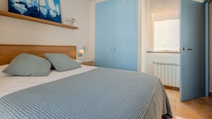 A bedroom with a bed, pillows, a nightstand, a lamp, a painting, and a wardrobe. - Costabravaforrent Can Riera (l'Escala)