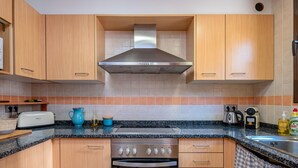 A modern kitchen with wooden cabinets, a stainless steel range hood, a built-in oven, and a granite countertop. - Costabravaforrent Can Riera (l'Escala)