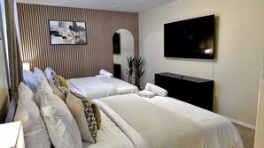 Quarto de hotel com duas camas, uma TV de tela plana, um quadro e um vaso de planta.