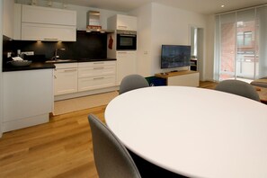 Eine moderne Küche mit weißen Schränken, einer schwarzen Arbeitsplatte und einem Essbereich mit rundem Tisch und Stühlen.