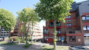 A multi-story residential building with balconies, a parking sign, and a car parked in front. - Sandwall 60, Whg. 12, Huus in Lee - Ferienwohnung mit 3 - Zimmern auf ca. 50m² (Wyk auf Föhr)