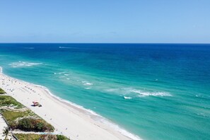 A beach with clear turquoise waters, a sandy shore, and a few umbrellas.