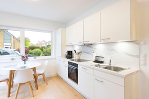 Una cocina moderna con armarios blancos, horno empotrado y un amplio ventanal con vistas a una zona residencial.