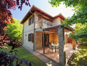 Une maison à deux étages dotée d’un balcon, d’une terrasse avec une table et des chaises, et d’une façade en briques.