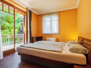 Une chambre avec un grand lit, une table de chevet, une fenêtre avec des rideaux et une vue sur la verdure.