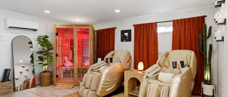 A room with two massage chairs, a red-lit sauna, a potted plant, and a cactus.