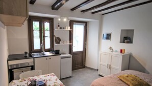 Una habitación compacta con kitchenette, una mesa de comedor, una cama y un ventanal pequeño.
