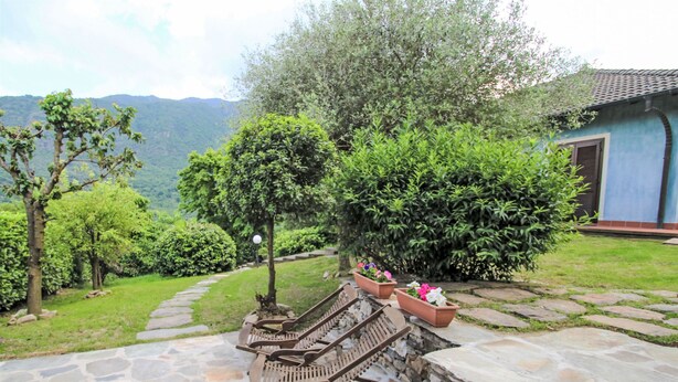 Una escalera de piedra conduce a un área de descanso con bancos, rodeada de abundante vegetación y vistas a las montañas.