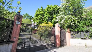 Una entrada protegida con un portón de metal, un cartel con un número y un árbol con flores blancas.