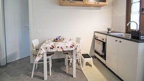 Cocina compacta con armarios blancos, encimera de madera y un pequeño comedor con mesa y sillas.