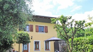 Una casa de dos pisos con fachada amarilla, contraventanas de madera y un camino de piedra que conduce a la entrada.