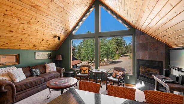 A cozy living room with a wooden ceiling, a fireplace, and large windows offering a view of the outdoors. - A/C, Views, Newly Renovated, Peaceful Retreat! (Durango)