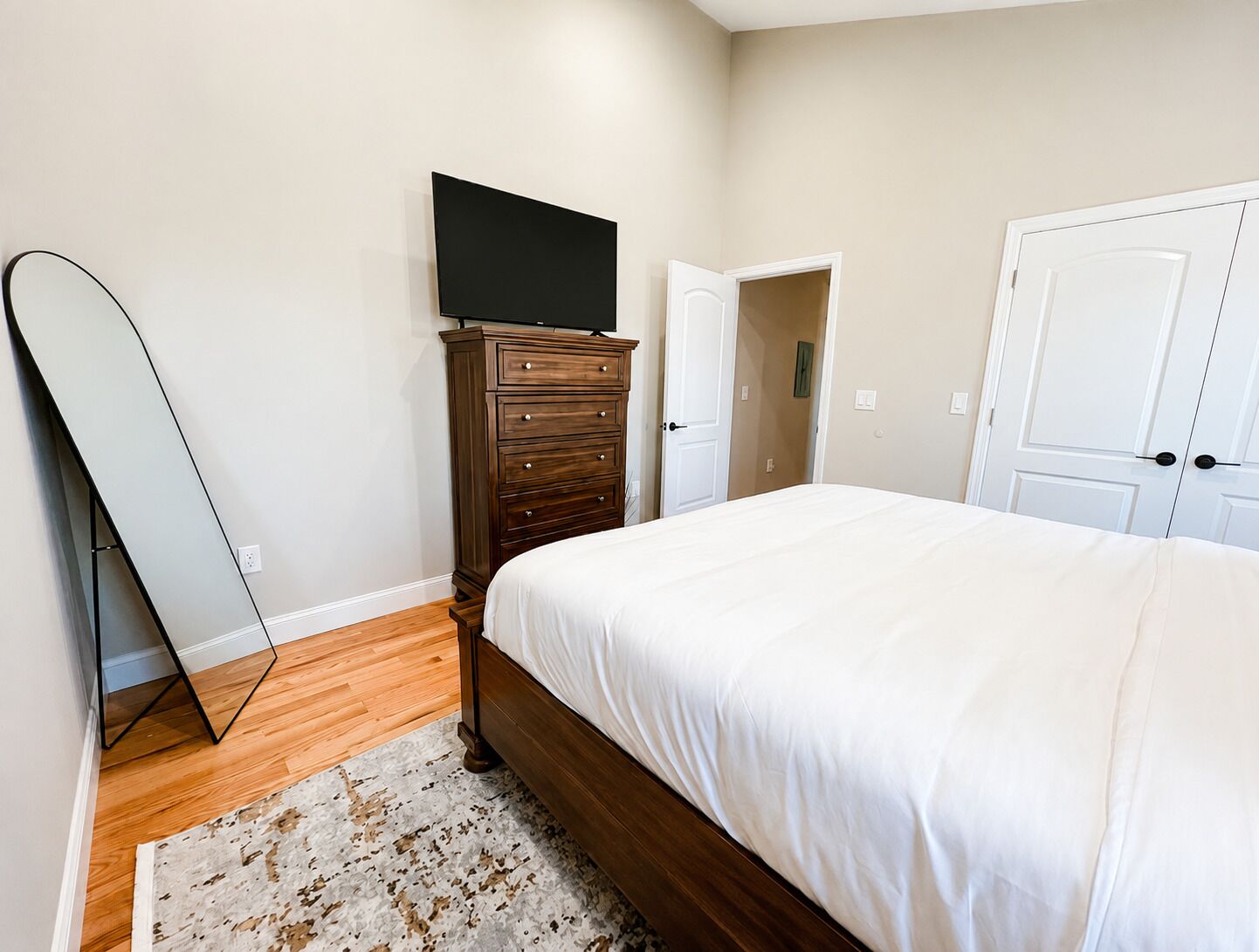 A bedroom with a bed, a dresser, a television, and a door.