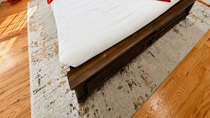 A neatly made bed with white and red bedding, a wooden headboard, and a large window with red curtains.