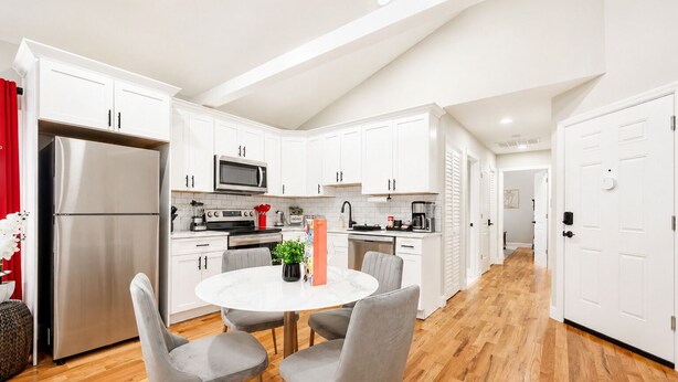 A modern kitchen with white cabinets, a stainless steel refrigerator, a microwave, and a dining area with a round table and two chairs.