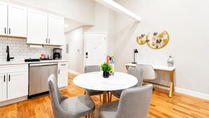 A modern kitchen with white cabinets, a coffee maker, and a dining area with a round table and grey chairs.