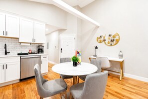 Een moderne keuken met witte kasten, een koffieapparaat en een eetgedeelte met een ronde tafel en grijze stoelen.