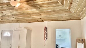Ein Zimmer mit Holzboden, einem weißen Kleiderschrank, einer Küchenzeile mit Schränken und einem Deckenventilator.