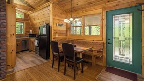A cabin interior with a dining area, kitchen, and a green door with a window. - Cabin in the mountains with hot tub! (Ellijay)